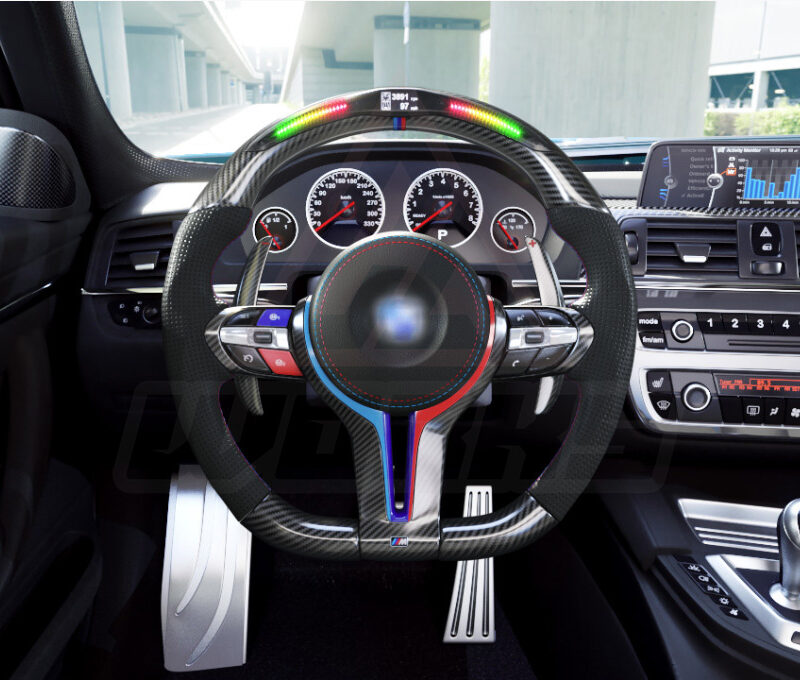 Front view of a BMW F chassis, M steering wheel in carbon fiber, extended paddle shifters, m color accents, black perforated leather, m color painted center trim, m color buttons, and led shift lights